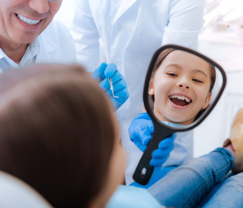 Kid in dentist chair looking at mirror smiling